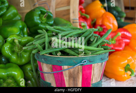 fresh green beans in wooden bushel basket and colorful peppers at the farmers market Stock Photo