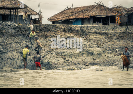 Sunderban, Bangladesh - circa July 2012: Native men work in mud near their houses and river in Sunderban, Bangladesh. Documentary editorial. Stock Photo