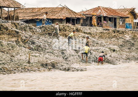 Sunderban, Bangladesh - circa July 2012: Six native men stand in mud and work near river and houses in Sunderban, Bangladesh. Documentary editorial. Stock Photo