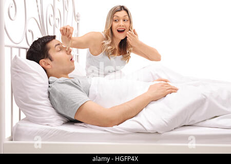 Man sleeping and snoring next to a woman putting a clothespin on his nose and laughing isolated on white background Stock Photo