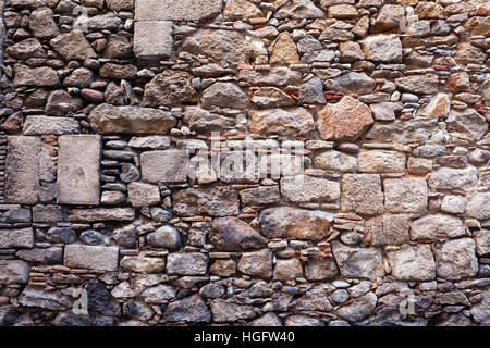Medieval stone wall background or texture made with different sizes of rough cut stones and some bricks between, Old Town of Girona in Spain Stock Photo