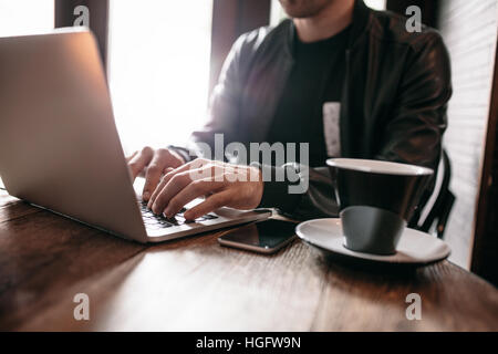 Close up shot of young man sitting at cafe and working on laptop. Stock Photo