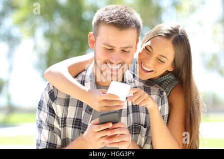 Portrait of two friends on line everyone with a smart phone outdoors in a park with a green background Stock Photo