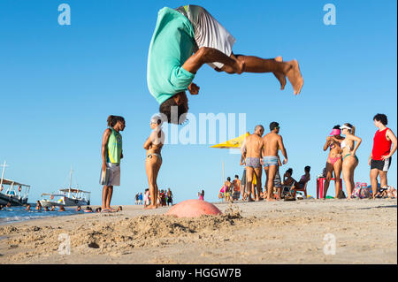 BAHIA, BRAZIL - FEBRUARY 6, 2016: Young Brazilian man performs acrobatic flip on the shore of a remote beach. Stock Photo
