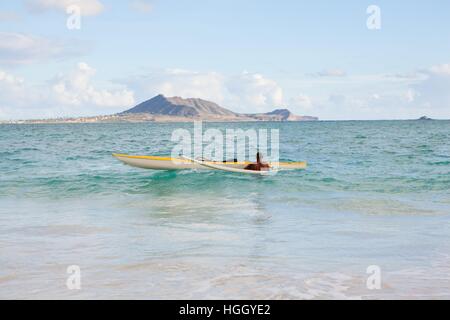 A man inspects his outrigger canoe in the surf before paddling out on his next tropical adventure. Stock Photo