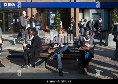 LONDON - SEPTEMBER 27, 2016: Unidentifed men reads a book on a bench with tourists in background. More than 15 million people visit London each year. Stock Photo
