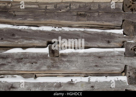 A festive winter background with weathered silvery grey horizontal sawn logs with snow in between.   Logs go towards the corner of building with log e Stock Photo