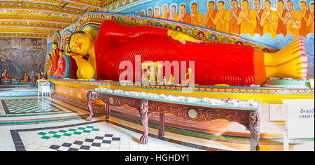 The giant statue of Reclining Buddha in Isurumuniya Rock Temple, surrounded by colorful paintings, patterns and altar with lotu Stock Photo