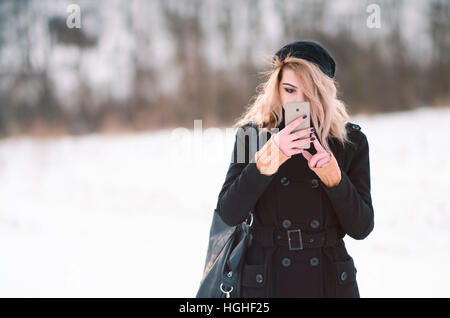 Young blond alternative girl in black clothes looking at phone Stock Photo