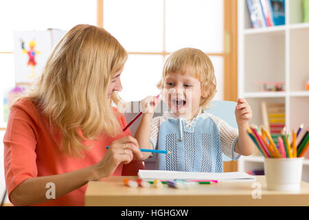 Happy family mother and kid son together paint. Woman helps child boy. Stock Photo