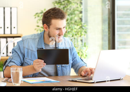 Entrepreneur working on line with a tablet and laptop in a desktop at office Stock Photo