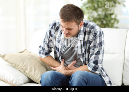 Man suffering stomach ache sitting on a couch in the living room at home Stock Photo