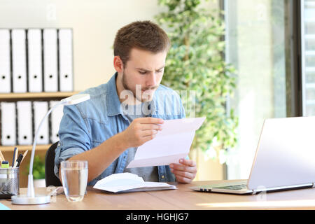 Serious entrepreneur working and reading a letter in a desktop at workplace Stock Photo