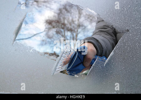 Man removing ice and snow from a car window with a ice scraper Stock Photo