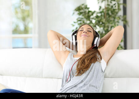 Front view portrait of a happy housewife relaxing listening music sitting on a sofa in the living room in a house Stock Photo