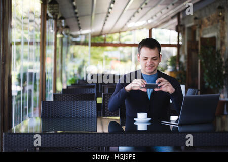 Young student man taking photo of a coffee cup and using laptop in canteen at the university or street cafe Stock Photo