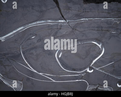 pattern of cracked ice in frozen puddle with details of silver bubbles and melting water below circular tramlines Stock Photo