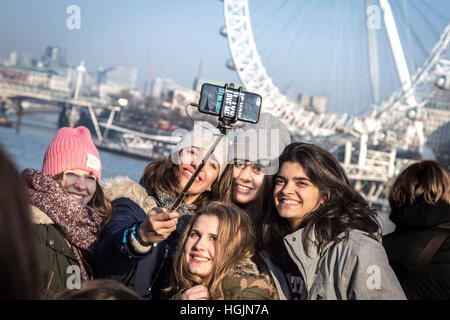 London, UK. 22nd January, 2017. UK Weather: Tourists on Westminster bridge take a group photo-selfie with London Eye background in the afternoon sun © Guy Corbishley/Alamy Live News