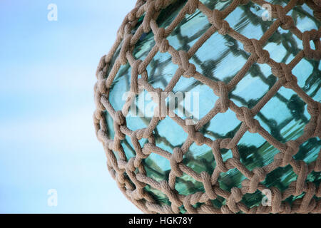 Turquoise green sea glass sphere tied up with nautical rope & knots against a blue sky. Stock Photo