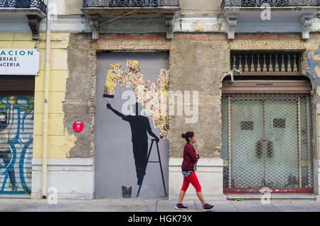 A woman walks past a street mural by spanish artist Pejac at the Soho bohemian arts quarter in Malaga, Andalusia, Spain Stock Photo