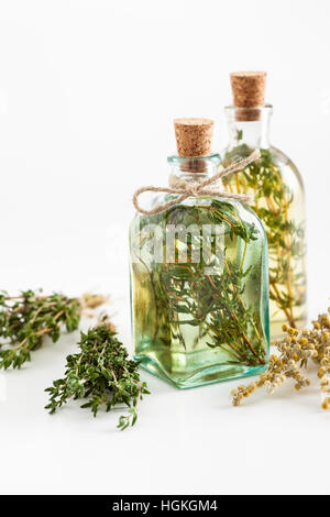 Bottles of thyme and rosemary essential oil or infusion and bunches of healthy herbs on white, herbal medicine. Stock Photo