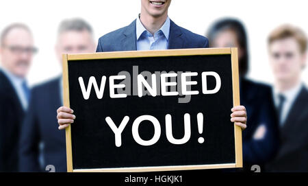 young businessman holding a sign with the words We Need You and group of people behind him Stock Photo