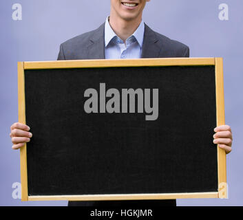 young man in suit holding up a black chalkboard Stock Photo