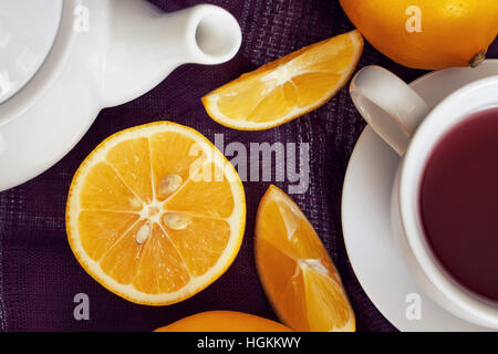 Lemon on purple tablecloth with cup of tea and teapot. Top view Stock Photo