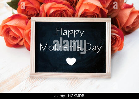 orange roses and blackboard with the words Happy Mothers Day on wooden table Stock Photo