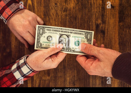 Woman offering one dollar bill to a man, top view of business office desk and hands exchanging cash Stock Photo