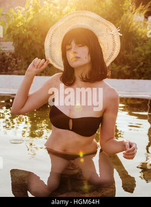 Back light portrait of a young woman wearing a black bikini in a natural pool