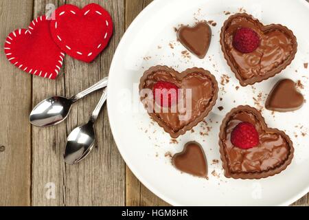 Heart shaped chocolate dessert cups with pudding and raspberries on plate with wood background Stock Photo