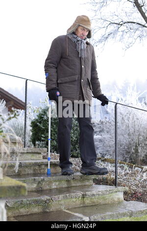 An Old man on crutches on icy stairs in winter Stock Photo