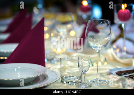Beautiful plates and glasses on a table in a restaurant on the background of colored lights of candles Stock Photo