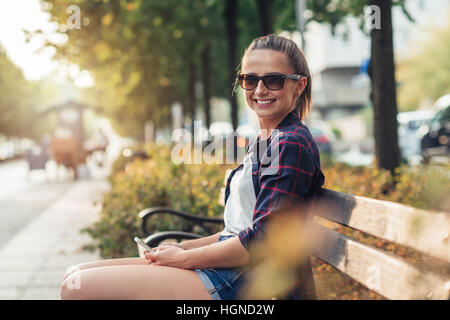 Young woman sitting on city bench with her cellphone Stock Photo