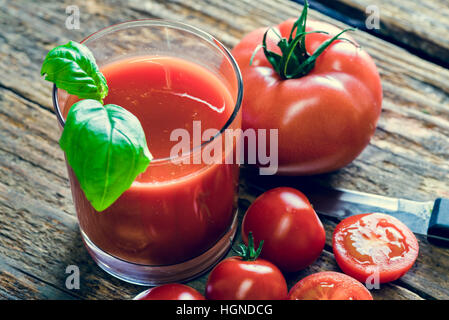 Glass of tomato juice and a few tmatos on wooden table Stock Photo