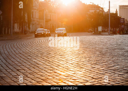 Vilnius, Lithuania  - July 8, 2016: Traffic On Zygimantu Street In Old Town. Moving Cars With Luminous Headlights On The Paved Road In Yellow Sunlight Stock Photo