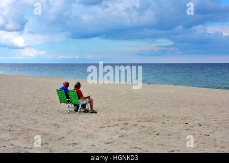 Older couple sitting on lounge chairs by sea and sandy beach Stock Photo