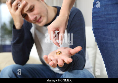 Closeup of a wife breaking up relationship leaving the wedding ring on the hand of her husband in a house interior Stock Photo