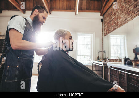 Side view shot of handsome young man getting haircut in salon. Hairstylist serving client in barber shop. Stock Photo