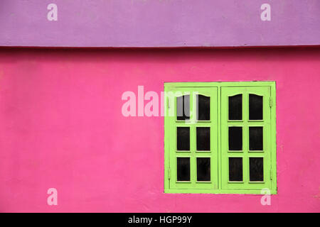 Close up of a brightly colored building with pink walls, lime green windows & purple roof, Caribbean. Stock Photo