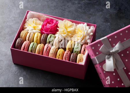 Colorful macaroons and flowers on stone table. Sweet macarons in gift box Stock Photo