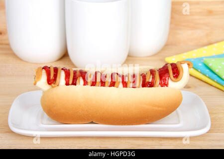 Banana with peanut butter and jelly in a hot dog bun served on a white rectangular plate, yellow, blue, green polka dot napkins and cups in background Stock Photo