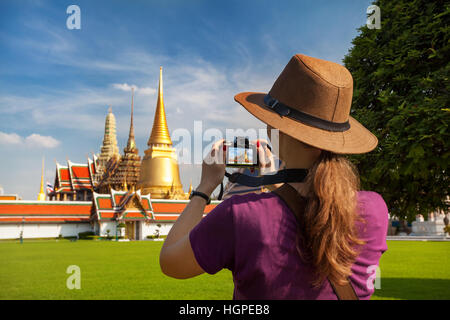 Woman tourist in hat taking a picture of Temple of the Emerald Buddha with Golden Stupa in Bangkok Stock Photo