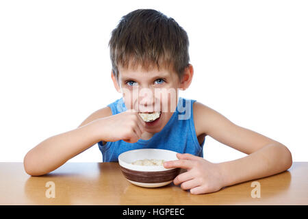 Happy boy eating porridge at the table isolated white Stock Photo