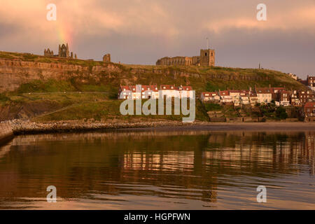 View of the East Cliff (houses, St. Mary's Church, abbey ruins and rainbow) reflected in the sea - Whitby, North Yorkshire, GB. Stock Photo