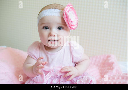 little girl in a pink dress sits on the bed Stock Photo