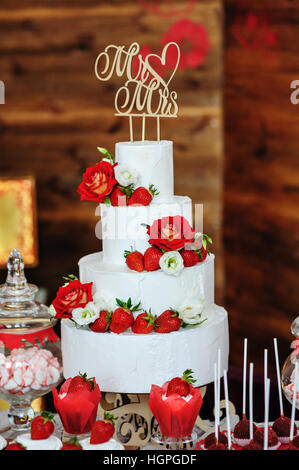 beautiful three-layered wedding cake decorated with red flowers Stock Photo