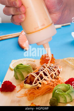 Chef adding sauce to a plate of salmon tartare served with avocado pear and red caviar or fish roe on a wooden board, close up of his hand Stock Photo