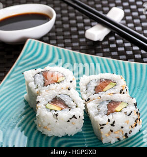 Close up view of four Urumaki sushi rolls served on blue plate with soy sauce and chopsticks Stock Photo